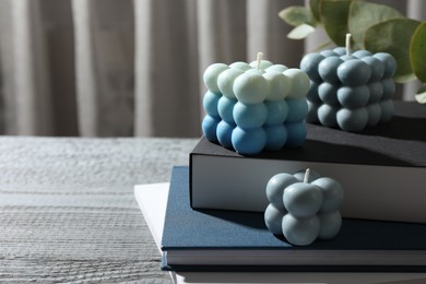 Photo of Stylish bubble candles and stack of books on grey wooden table, closeup. Space for text