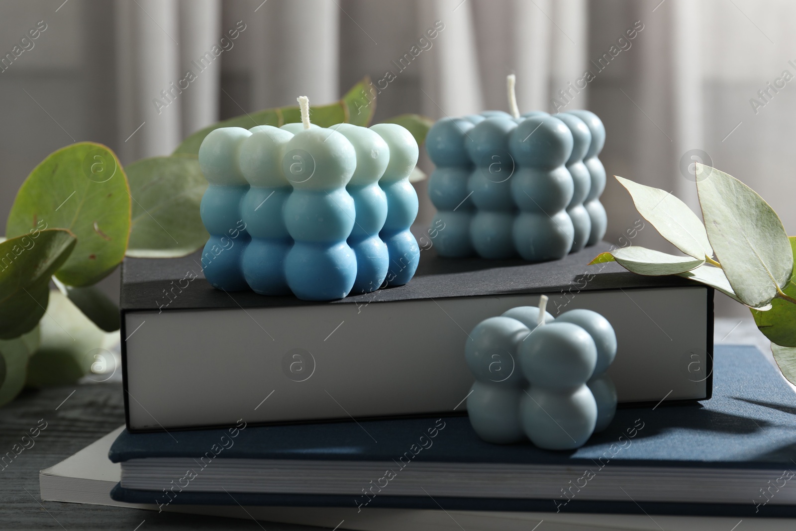 Photo of Stylish bubble candles and stack of books on grey wooden table, closeup