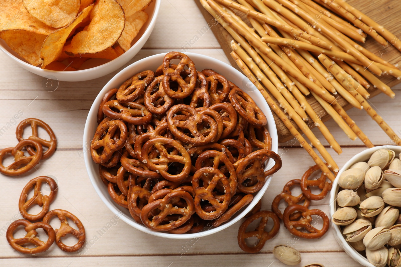 Photo of Delicious pretzel crackers and other snacks on white wooden table, flat lay