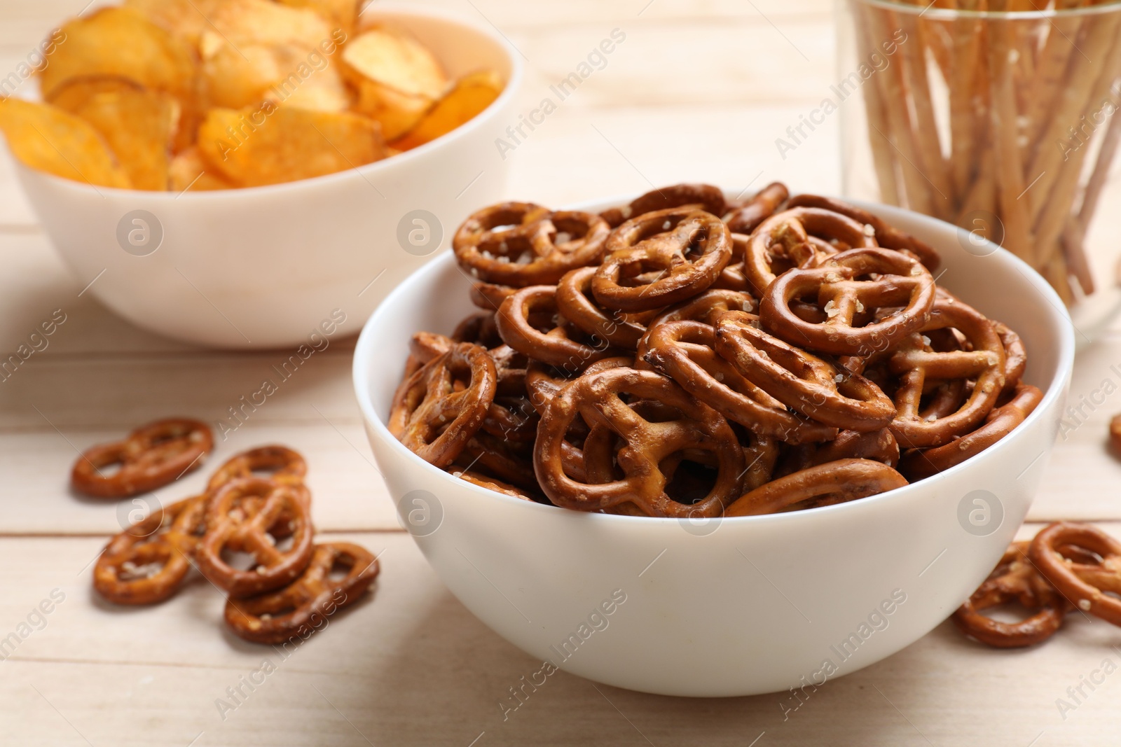 Photo of Delicious pretzel crackers and other snacks on white wooden table, closeup