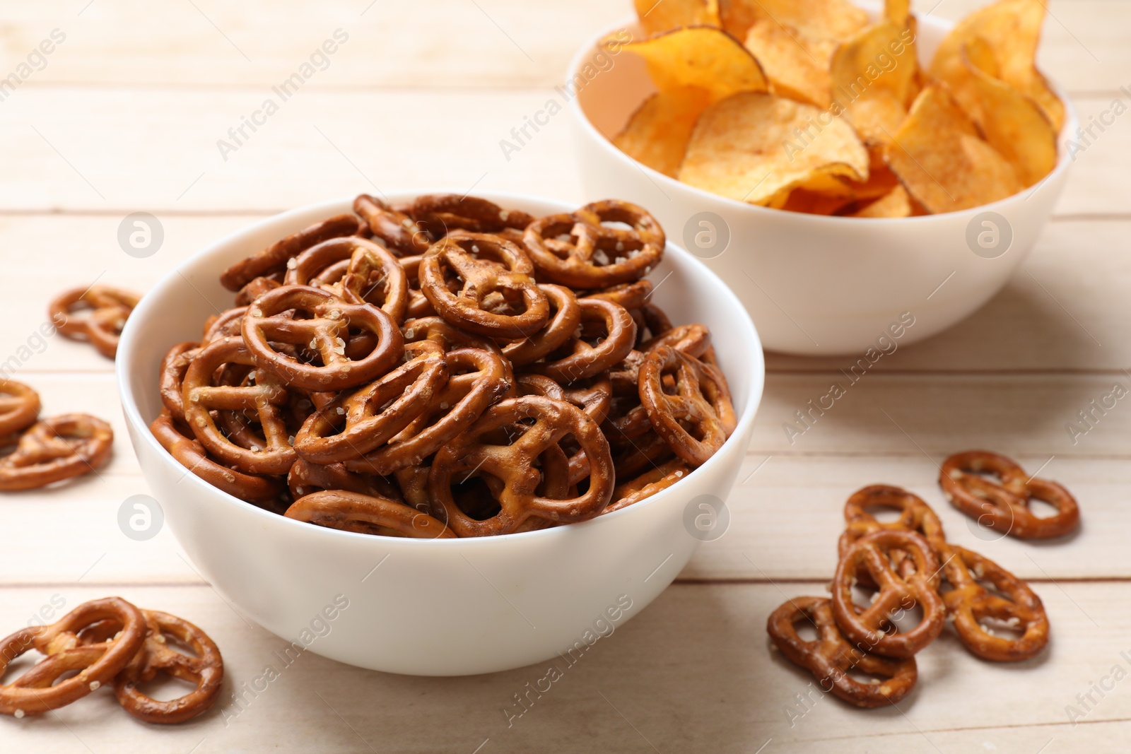 Photo of Delicious pretzel crackers and chips on white wooden table, closeup