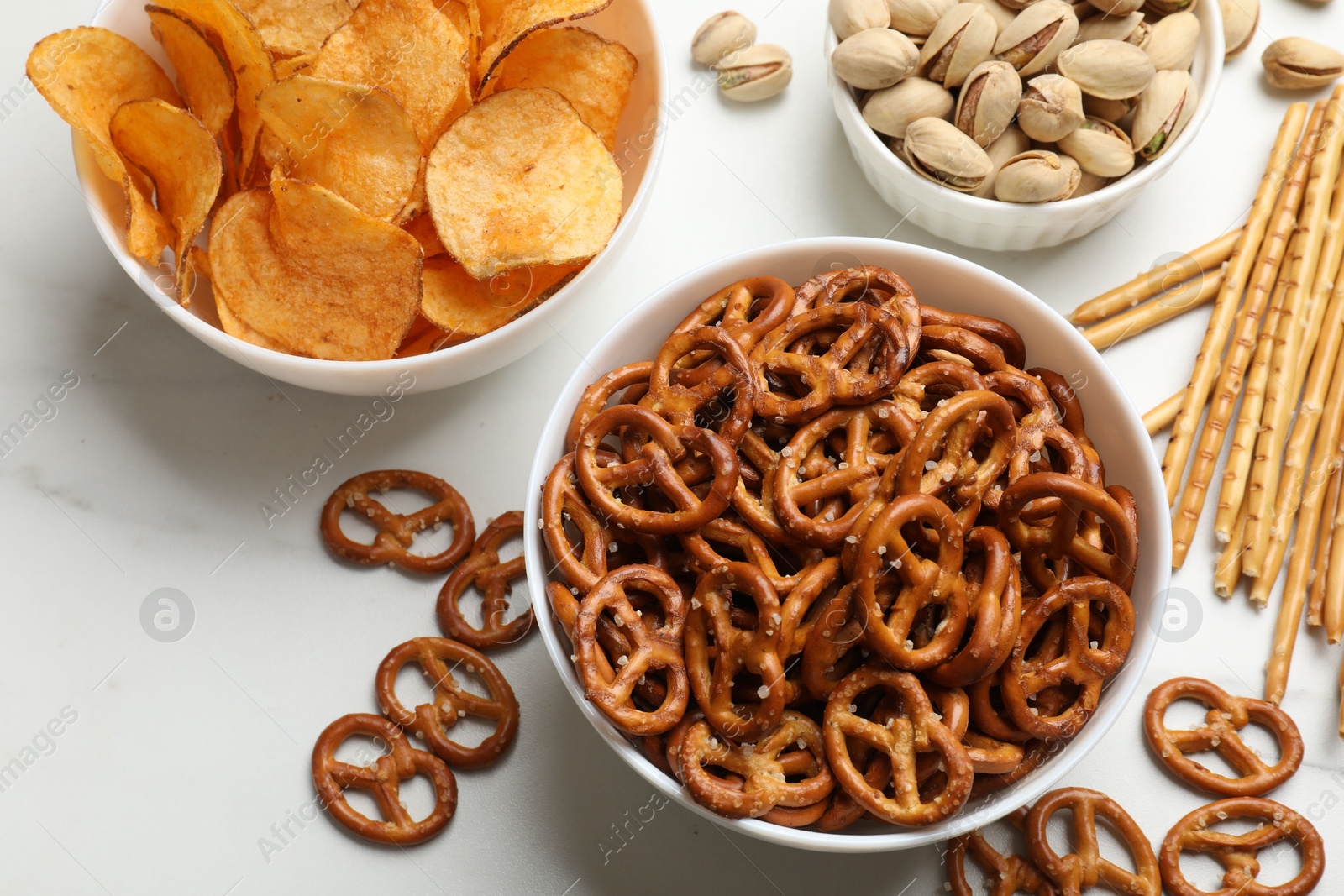 Photo of Delicious pretzel crackers and other snacks on white table, flat lay