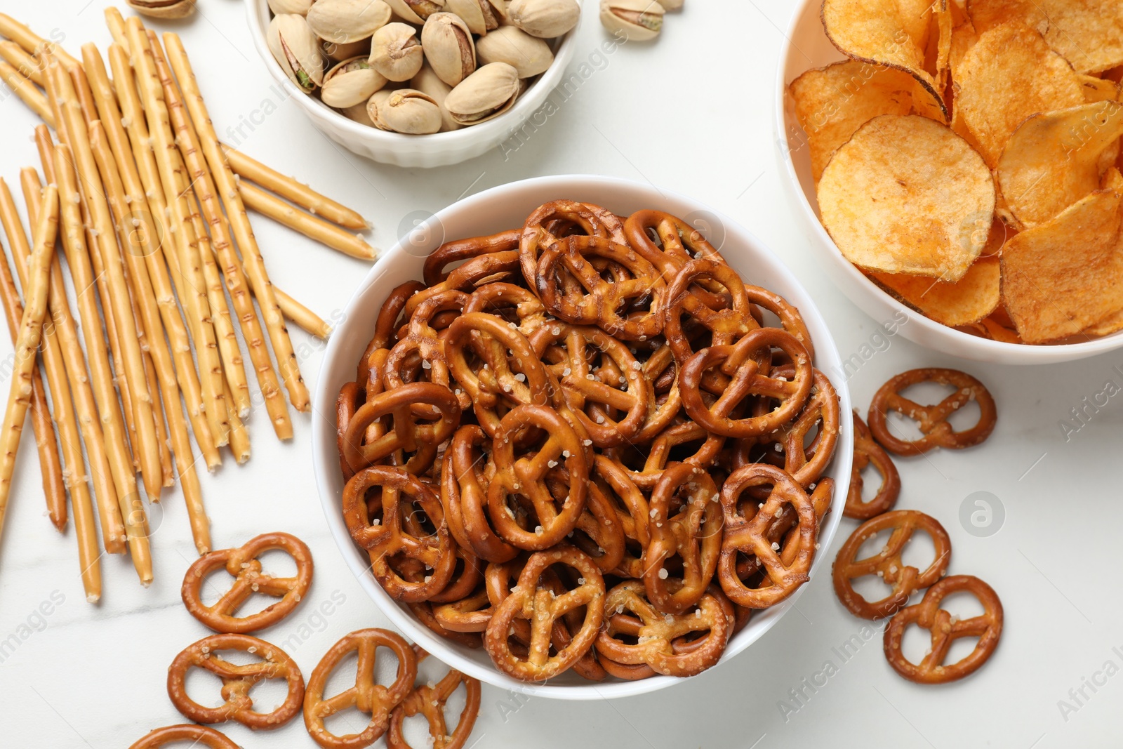 Photo of Delicious pretzel crackers and other snacks on white table, flat lay