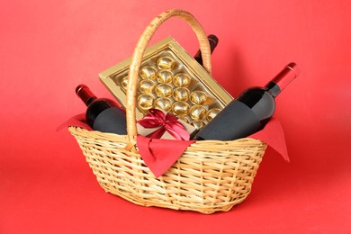 Photo of Wicker gift basket with wine on red background