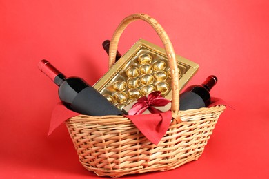 Photo of Wicker gift basket with wine on red background