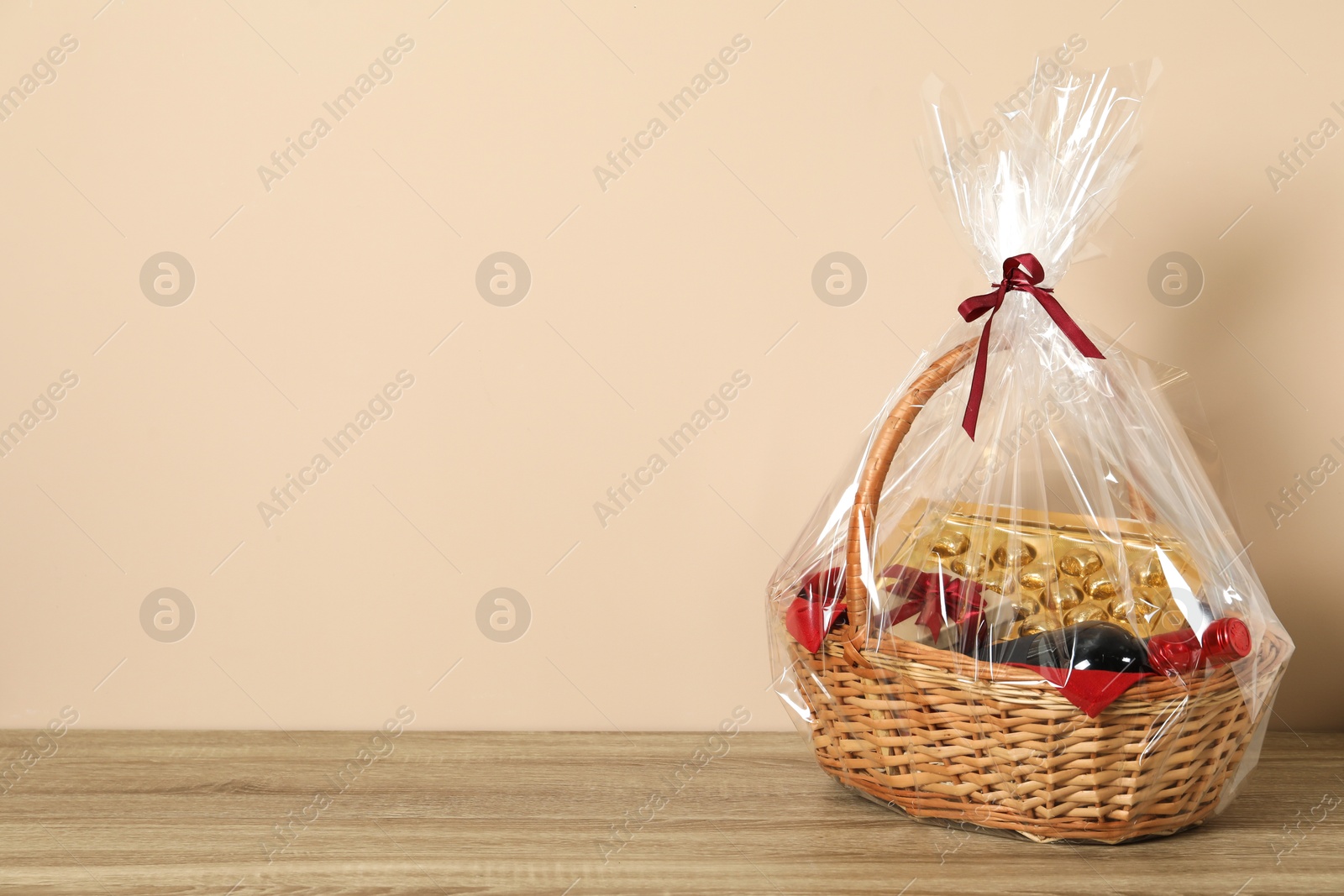 Photo of Wicker gift basket on wooden table against beige background. Space for text