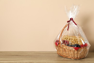 Photo of Wicker gift basket on wooden table against beige background. Space for text