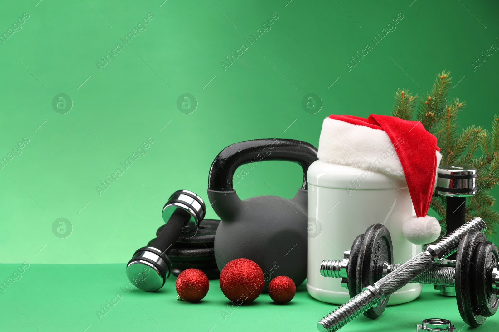 Photo of Dumbbells, kettlebell, container with supplement and Christmas decor on green background. Space for text