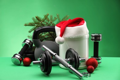 Photo of Dumbbells, kettlebell, container with supplement and Christmas decor on green background