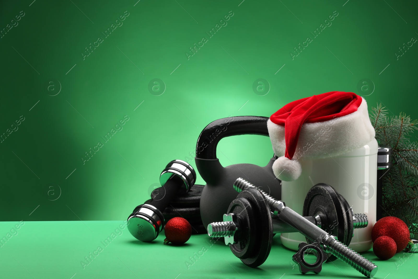 Photo of Dumbbells, kettlebell, container with supplement and Christmas decor on green background. Space for text