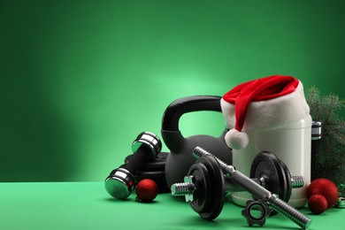 Photo of Dumbbells, kettlebell, container with supplement and Christmas decor on green background. Space for text