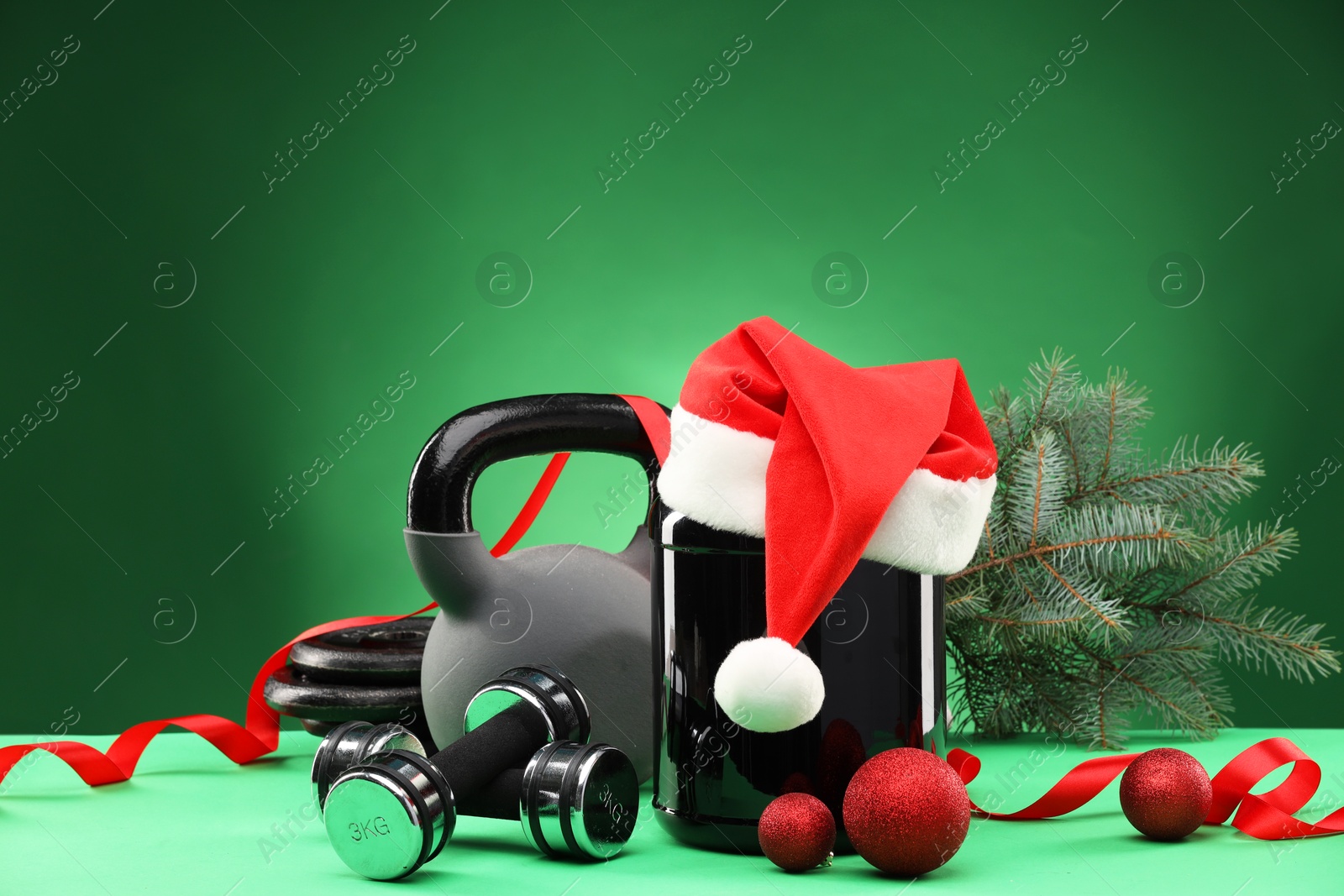 Photo of Dumbbells, kettlebell, container with supplement and Christmas decor on green background. Space for text