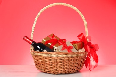 Wicker gift basket with wine on light marble table against color background