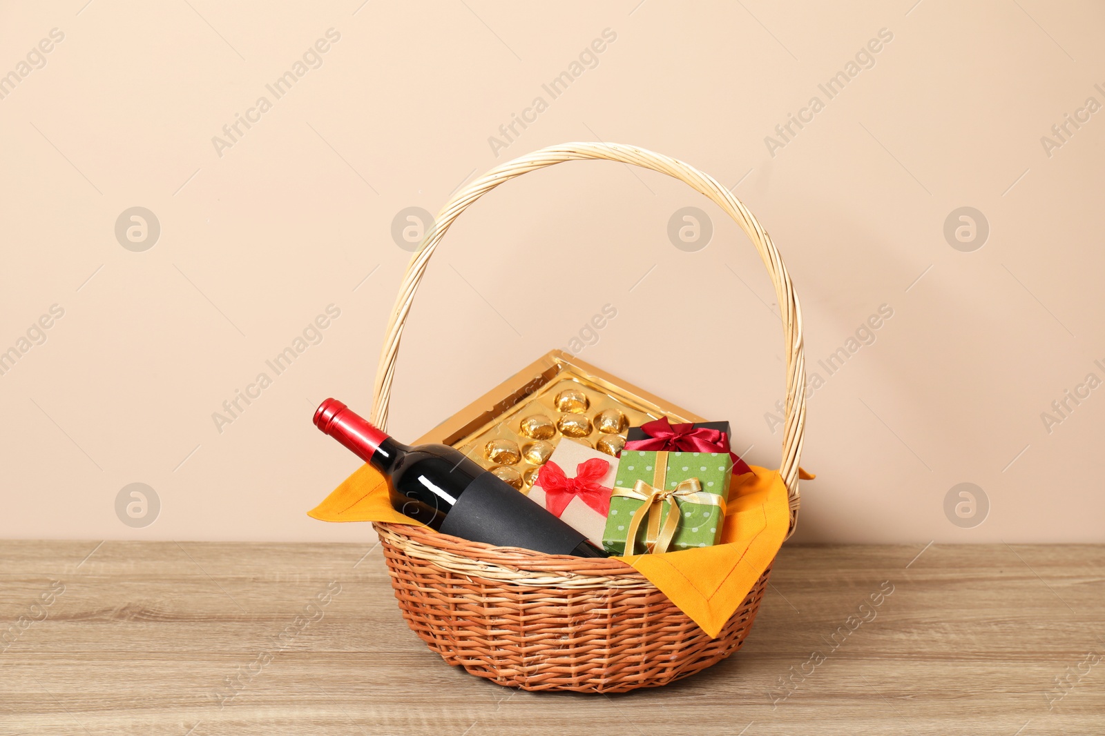 Photo of Wicker gift basket with wine on wooden table against beige background