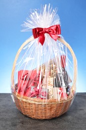 Photo of Wicker gift basket with wine on grey textured table against light blue background