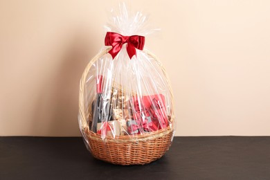 Photo of Wicker gift basket with wine on black textured table against beige background