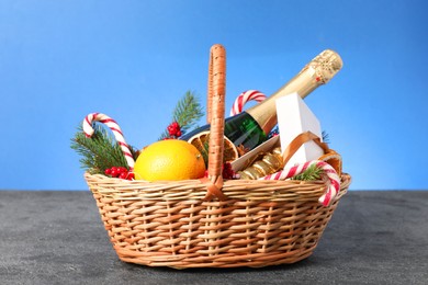 Wicker gift basket with sparkling wine and Christmas decor on grey textured table against light blue background