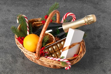 Wicker gift basket with sparkling wine and Christmas decor on grey textured table