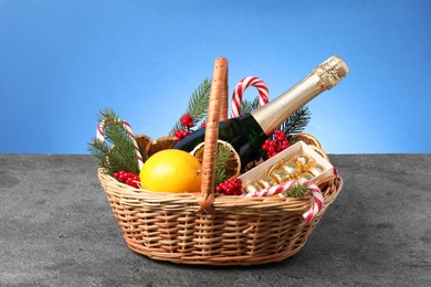 Wicker gift basket with sparkling wine and Christmas decor on grey textured table against light blue background