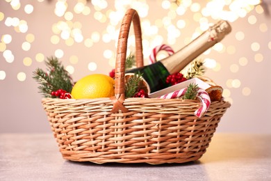 Wicker gift basket with sparkling wine and Christmas decor on light textured table