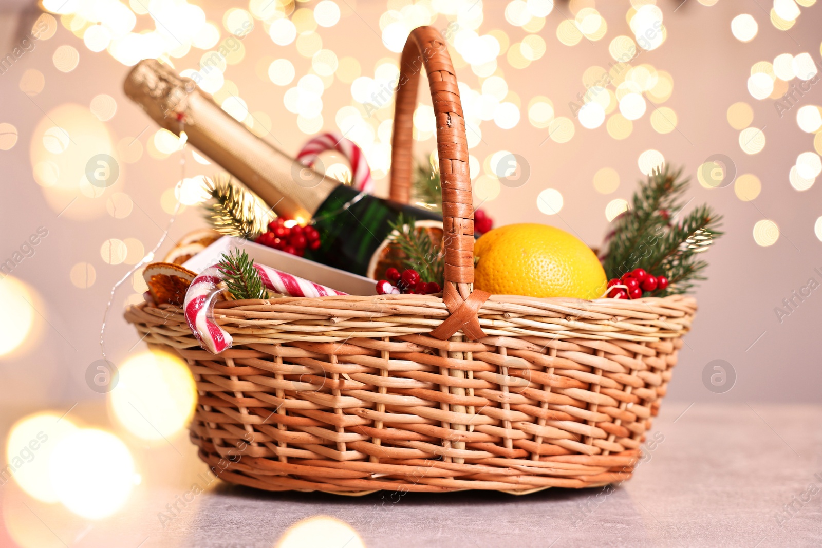 Photo of Wicker gift basket with sparkling wine and Christmas decor on light textured table