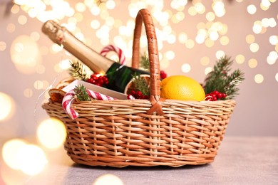 Wicker gift basket with sparkling wine and Christmas decor on light textured table