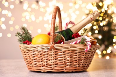 Wicker gift basket with sparkling wine and Christmas decor on light textured table