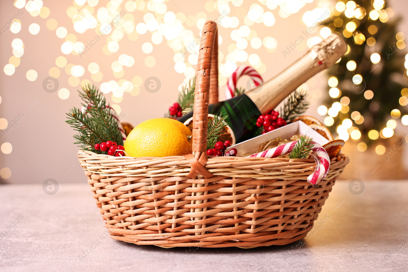 Photo of Wicker gift basket with sparkling wine and Christmas decor on light textured table