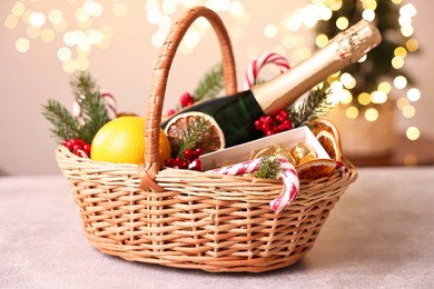 Photo of Wicker gift basket with sparkling wine and Christmas decor on light textured table