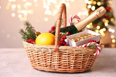 Wicker gift basket with sparkling wine and Christmas decor on light textured table