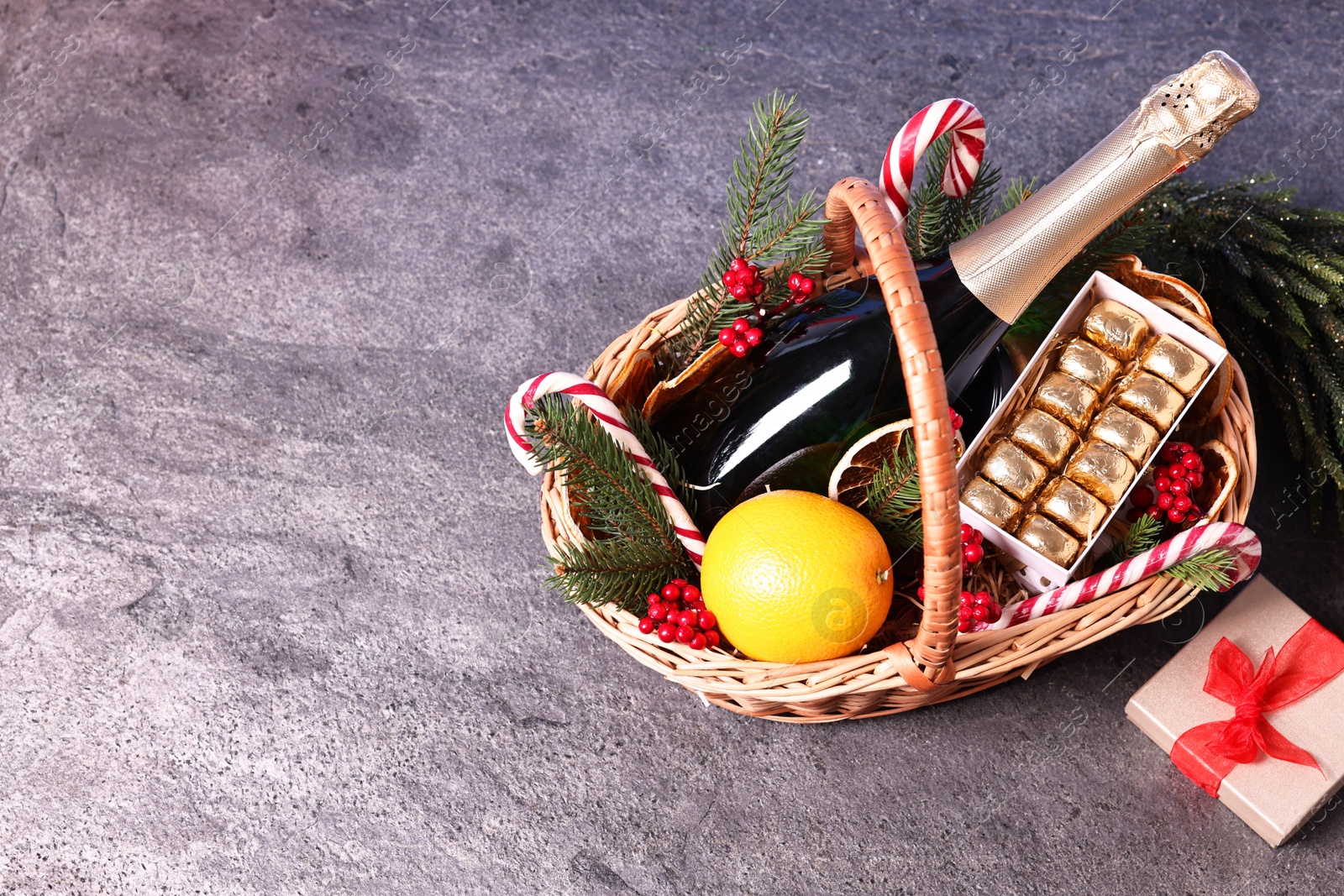 Photo of Wicker gift basket with sparkling wine and Christmas decor on grey textured table, space for text