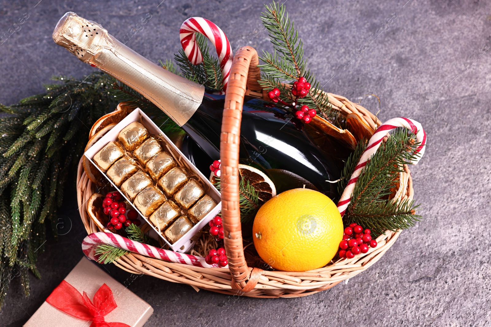 Photo of Wicker gift basket with sparkling wine and Christmas decor on grey textured table