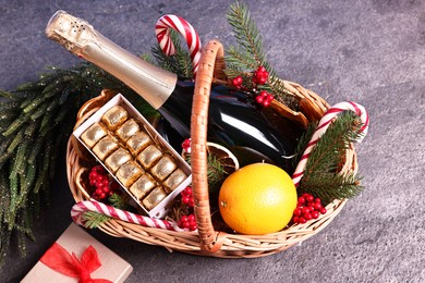 Photo of Wicker gift basket with sparkling wine and Christmas decor on grey textured table