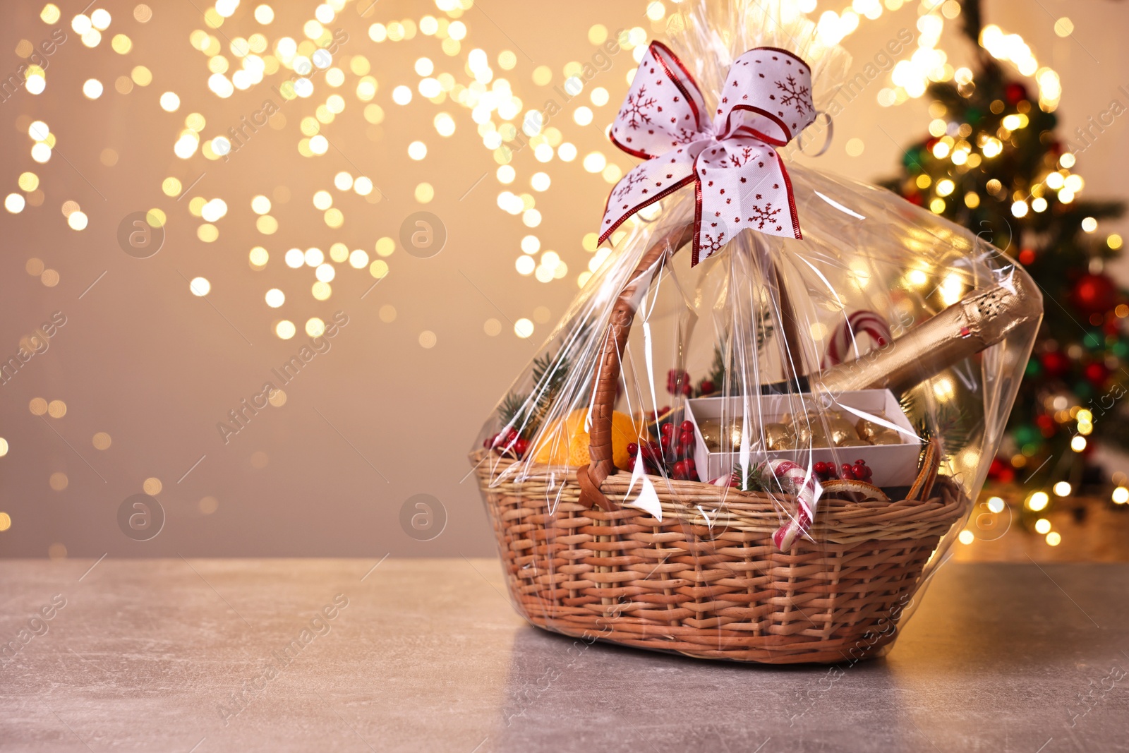 Photo of Wicker gift basket with sparkling wine and Christmas decor on light grey textured table, space for text