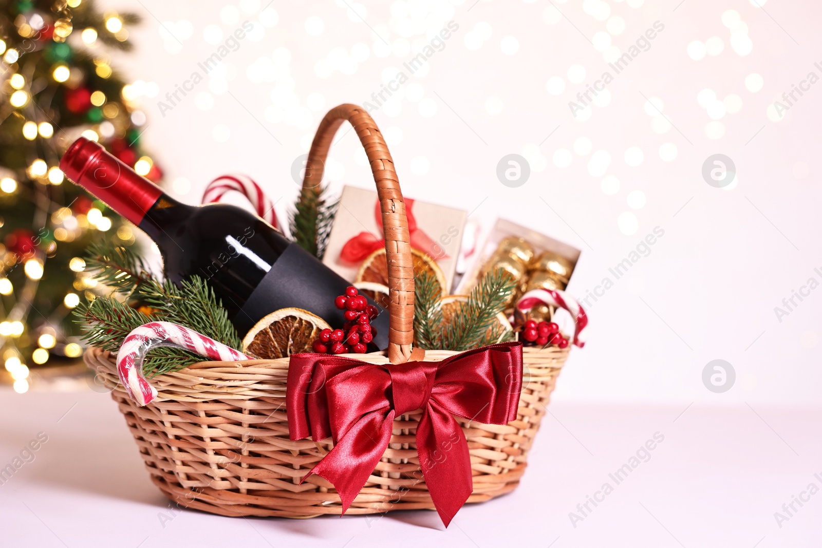 Photo of Wicker gift basket with wine and Christmas decor on light table