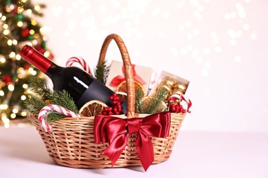 Photo of Wicker gift basket with wine and Christmas decor on light table