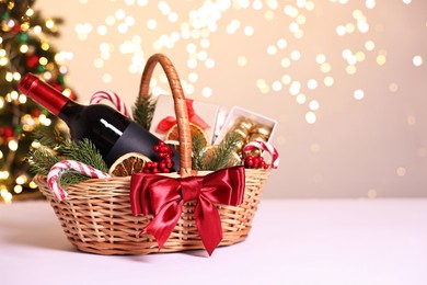 Photo of Wicker gift basket with wine and Christmas decor on light table, space for text