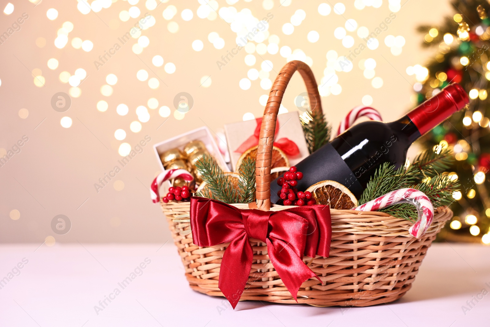 Photo of Wicker gift basket with wine and Christmas decor on light table, space for text