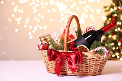 Photo of Wicker gift basket with wine and Christmas decor on light table, space for text