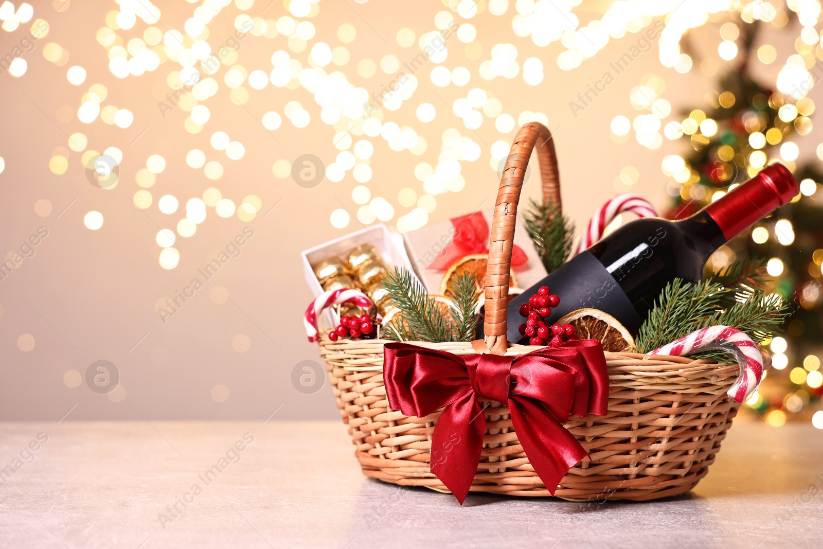 Photo of Wicker gift basket with wine and Christmas decor on light textured table, space for text