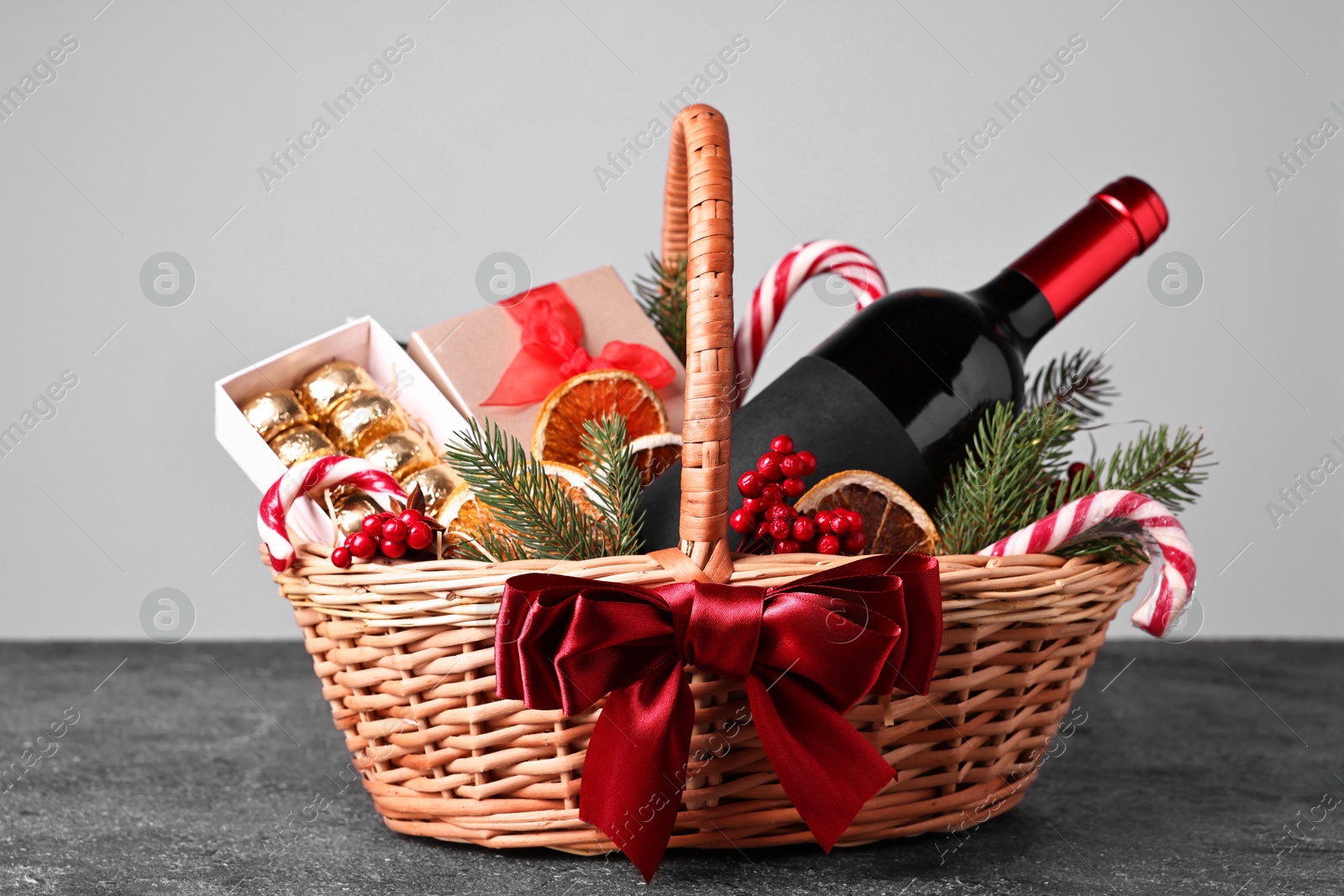 Photo of Wicker gift basket with wine and Christmas decor on grey textured table