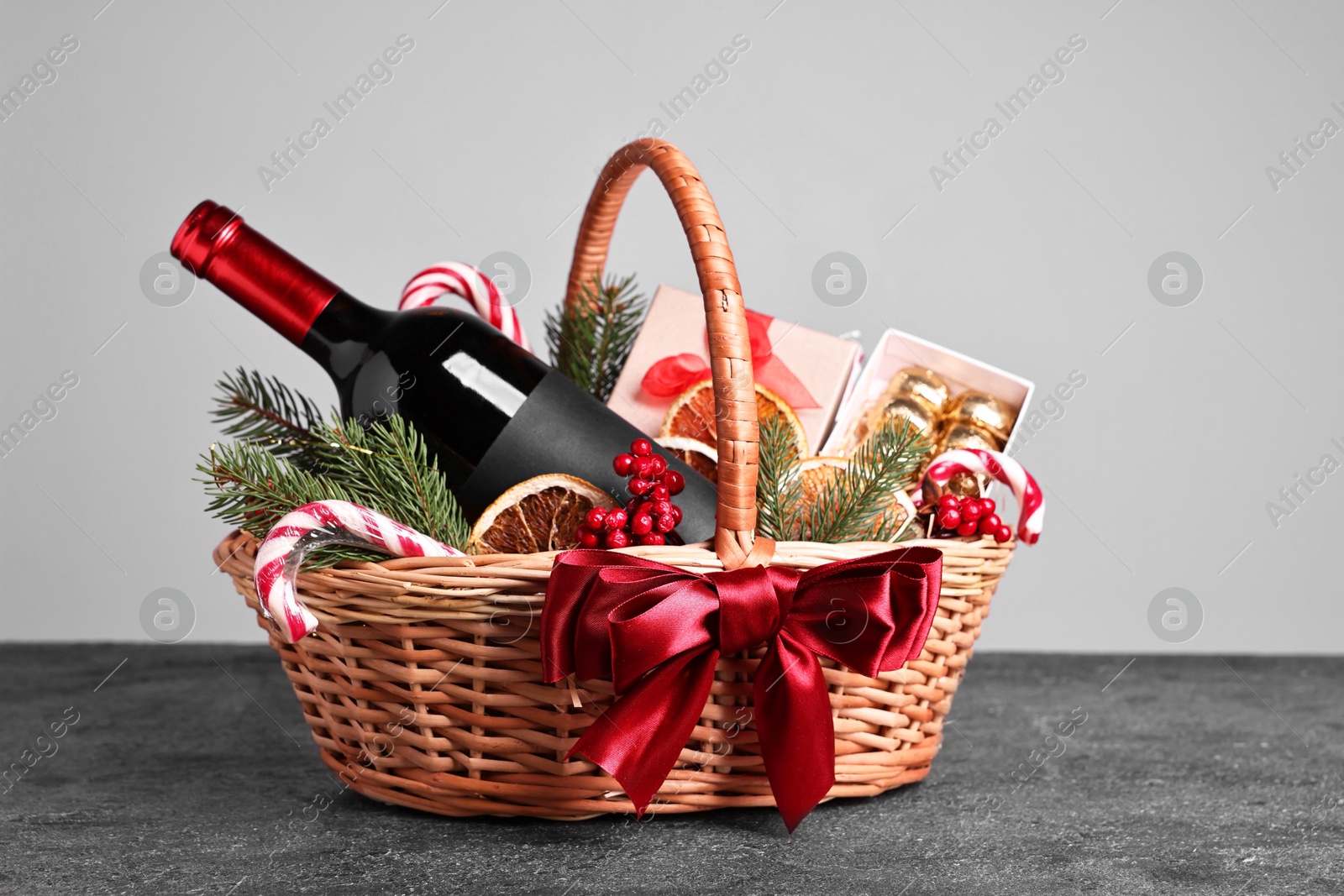 Photo of Wicker gift basket with wine and Christmas decor on grey textured table