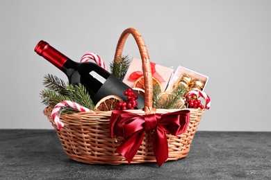 Wicker gift basket with wine and Christmas decor on grey textured table