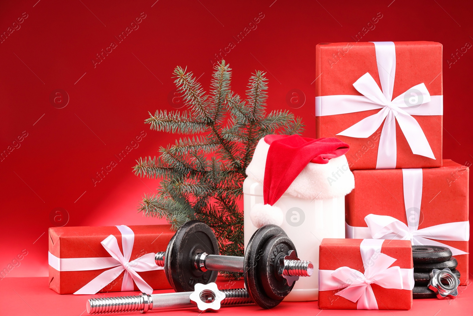 Photo of Dumbbells, container with supplement and Christmas decor on red background. Space for text