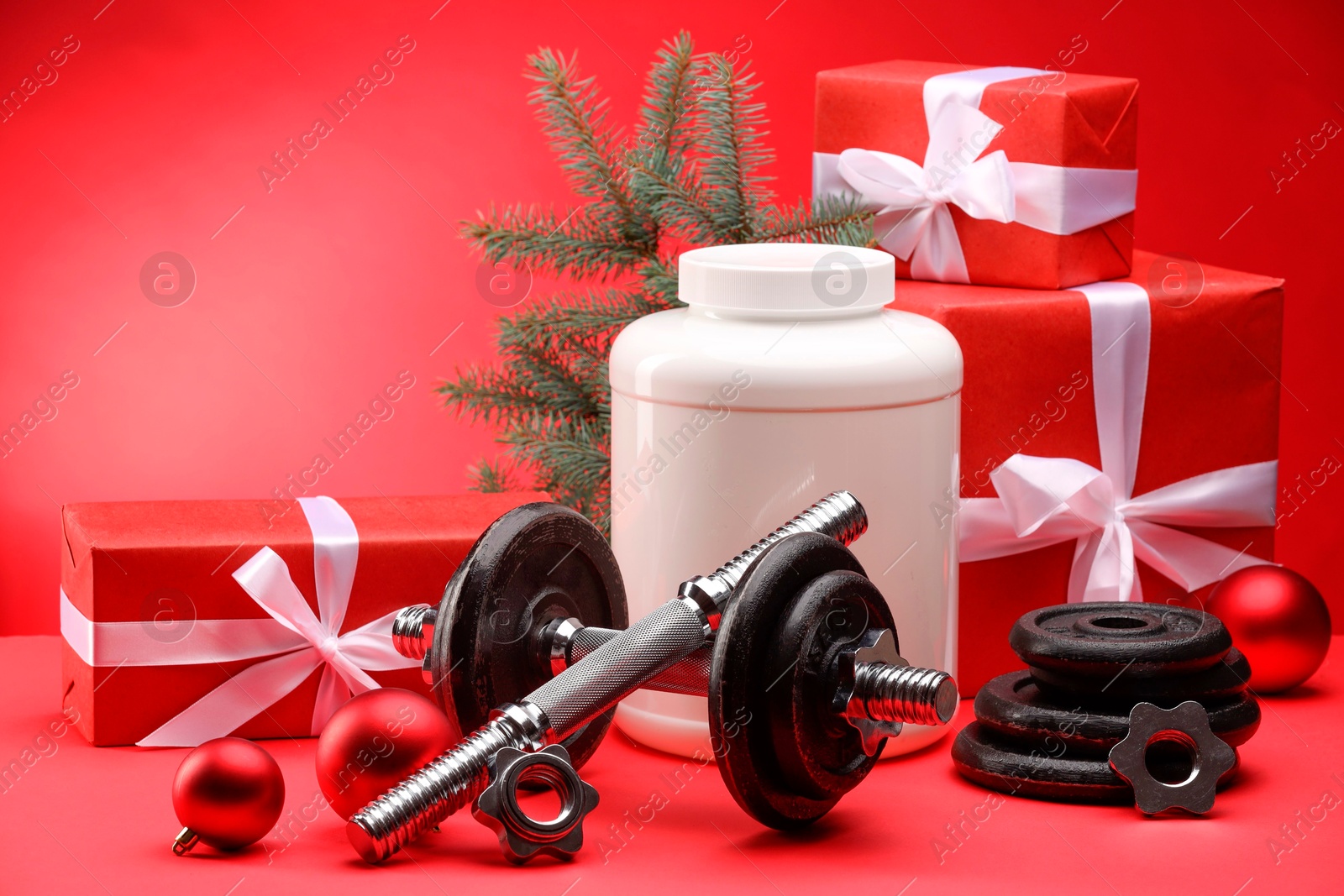 Photo of Dumbbells, container with supplement and Christmas decor on red background