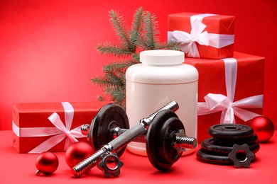 Photo of Dumbbells, container with supplement and Christmas decor on red background