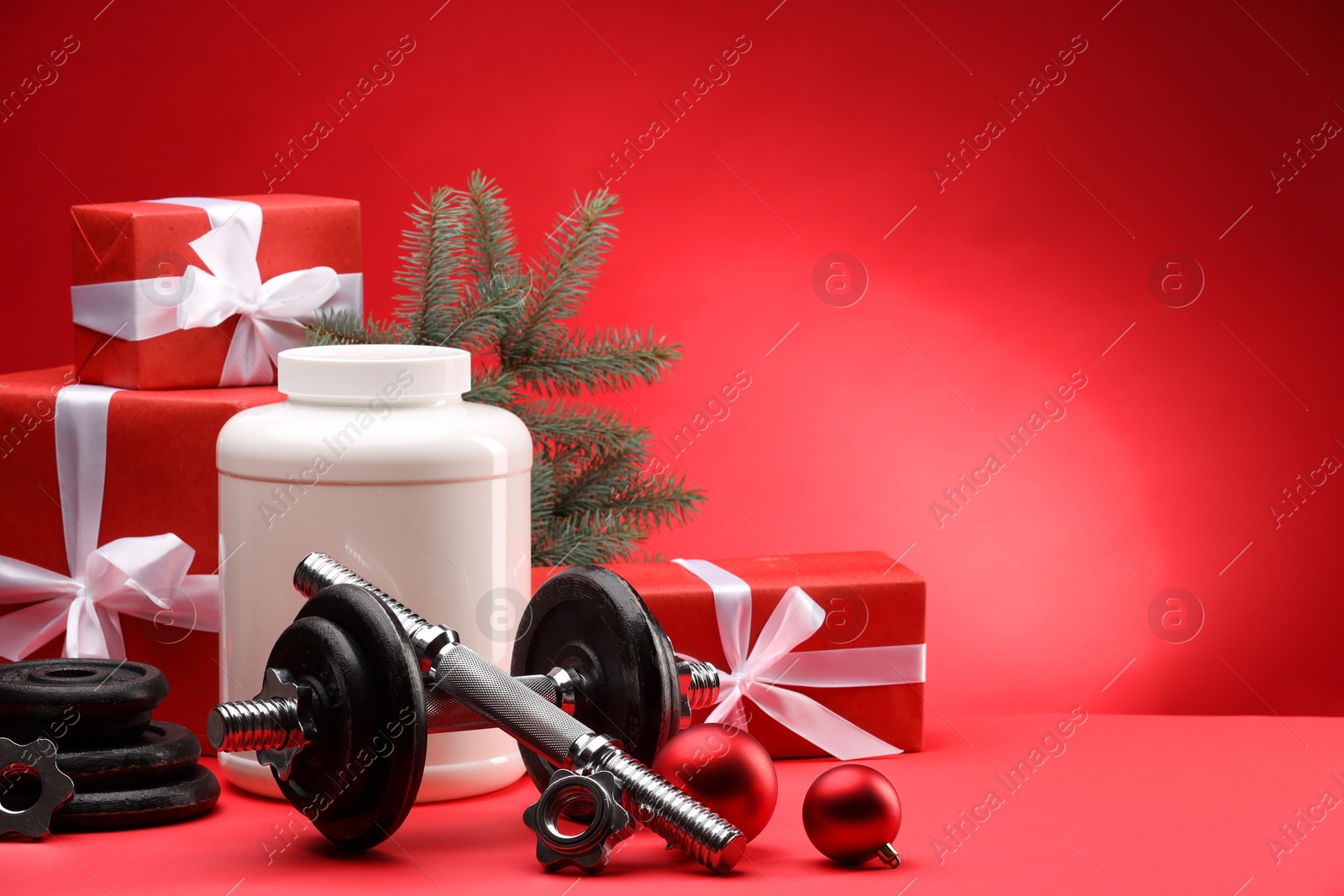 Photo of Dumbbells, container with supplement and Christmas decor on red background. Space for text