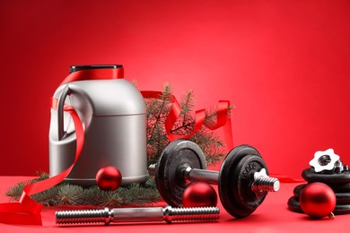 Photo of Dumbbells, container with supplement and Christmas decor on red background. Space for text