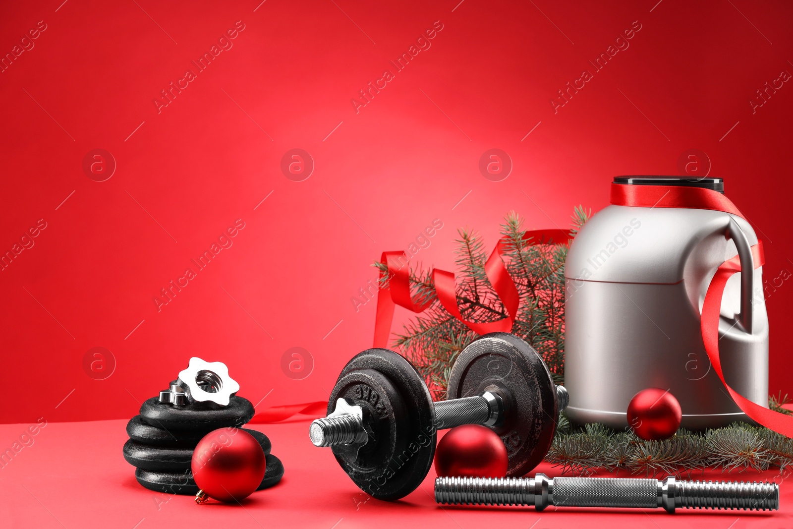 Photo of Dumbbells, container with supplement and Christmas decor on red background. Space for text