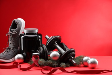 Photo of Dumbbells, container with supplement, sneakers and Christmas decor on red background. Space for text